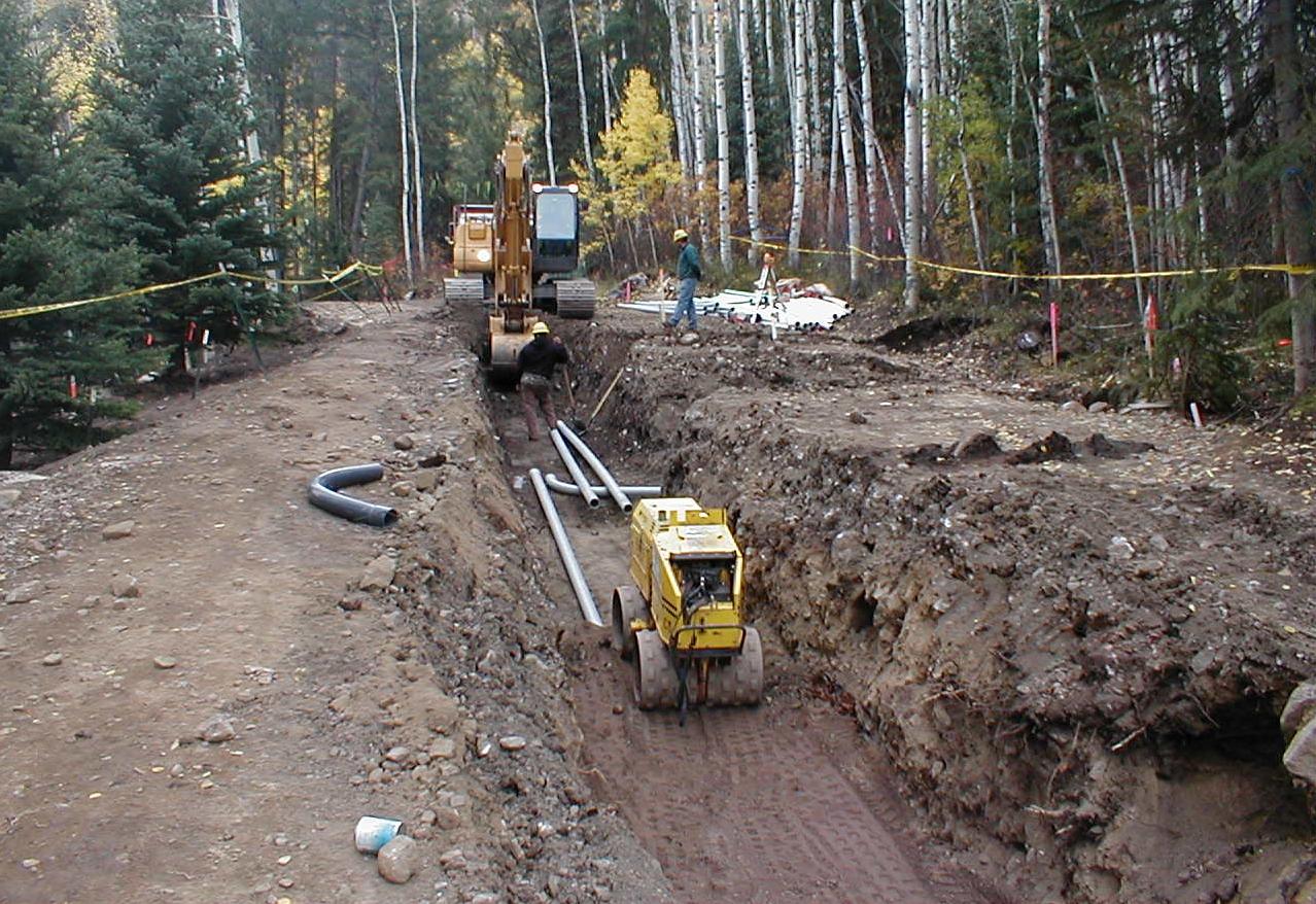 Contractor excavating a trench between survey lath and flagging.